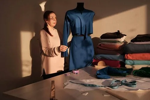 A designer works at golden hour on a blue dress mounted on a mannequin